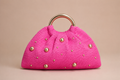 Pink handbag with gold studs on a beige background