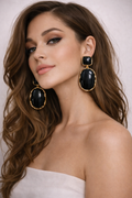 Woman wearing large black and gold earrings against a neutral background