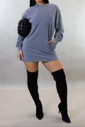 Woman wearing a gray sweater dress and black knee-high boots on a plain background