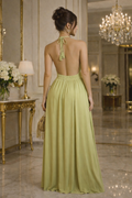 Woman in a green evening gown standing in an elegant room with chandeliers and floral arrangements.