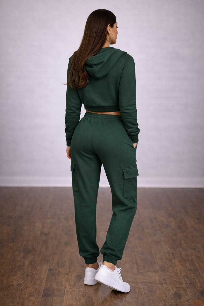 Person wearing a green tracksuit standing in a room with a plain background