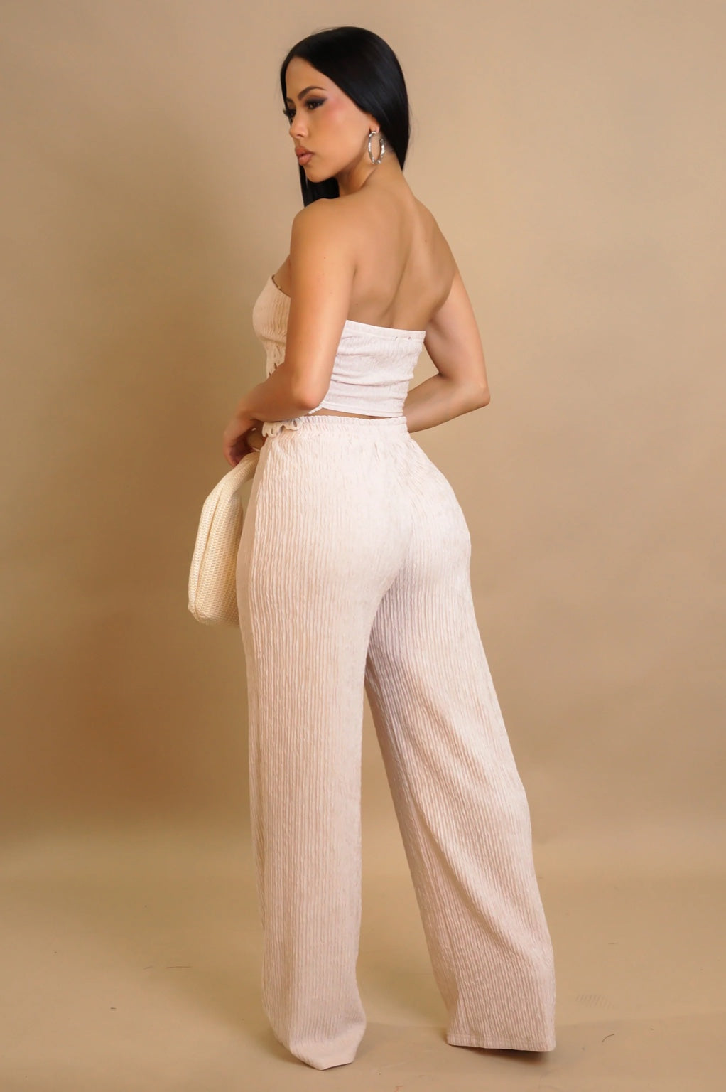 Woman wearing a beige strapless top and wide-leg pants against a beige background