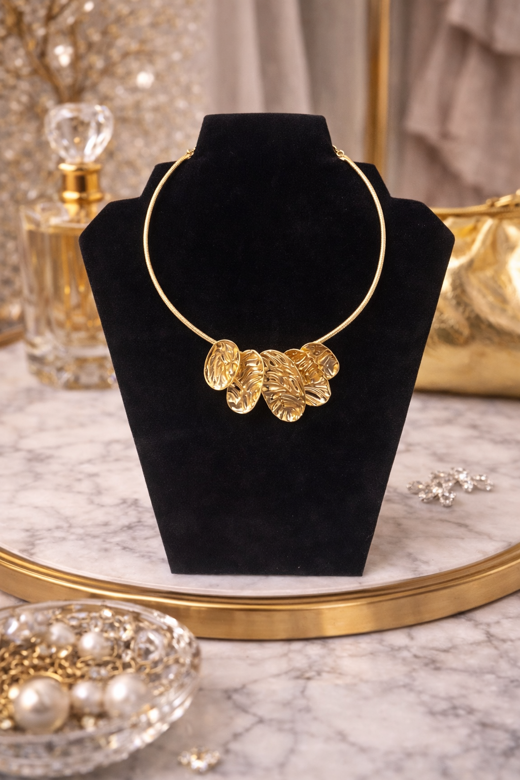 Gold necklace on a black velvet stand with a marble surface and decorative items in the background