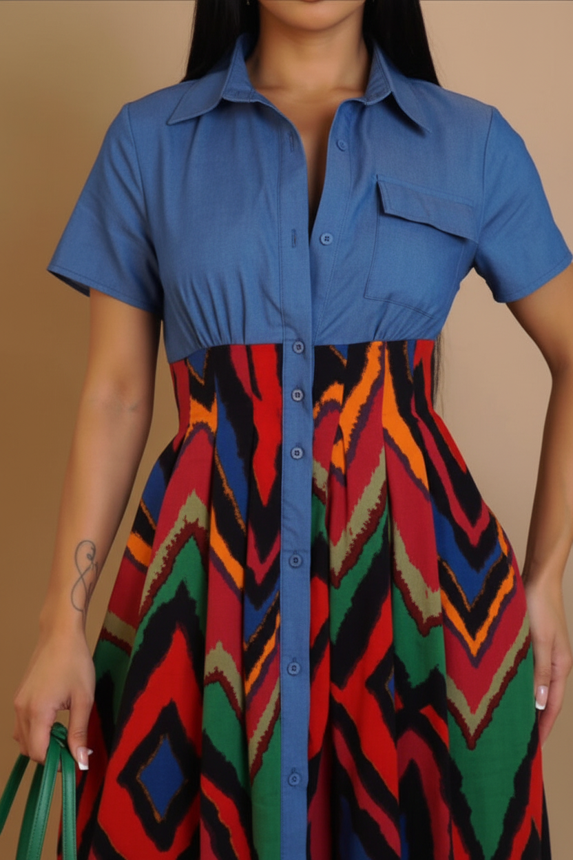 A woman wearing a short-sleeve button-front dress with a solid blue upper section and a colorful geometric patterned lower skirt in red, green, black, orange, and beige, against a plain beige background.
