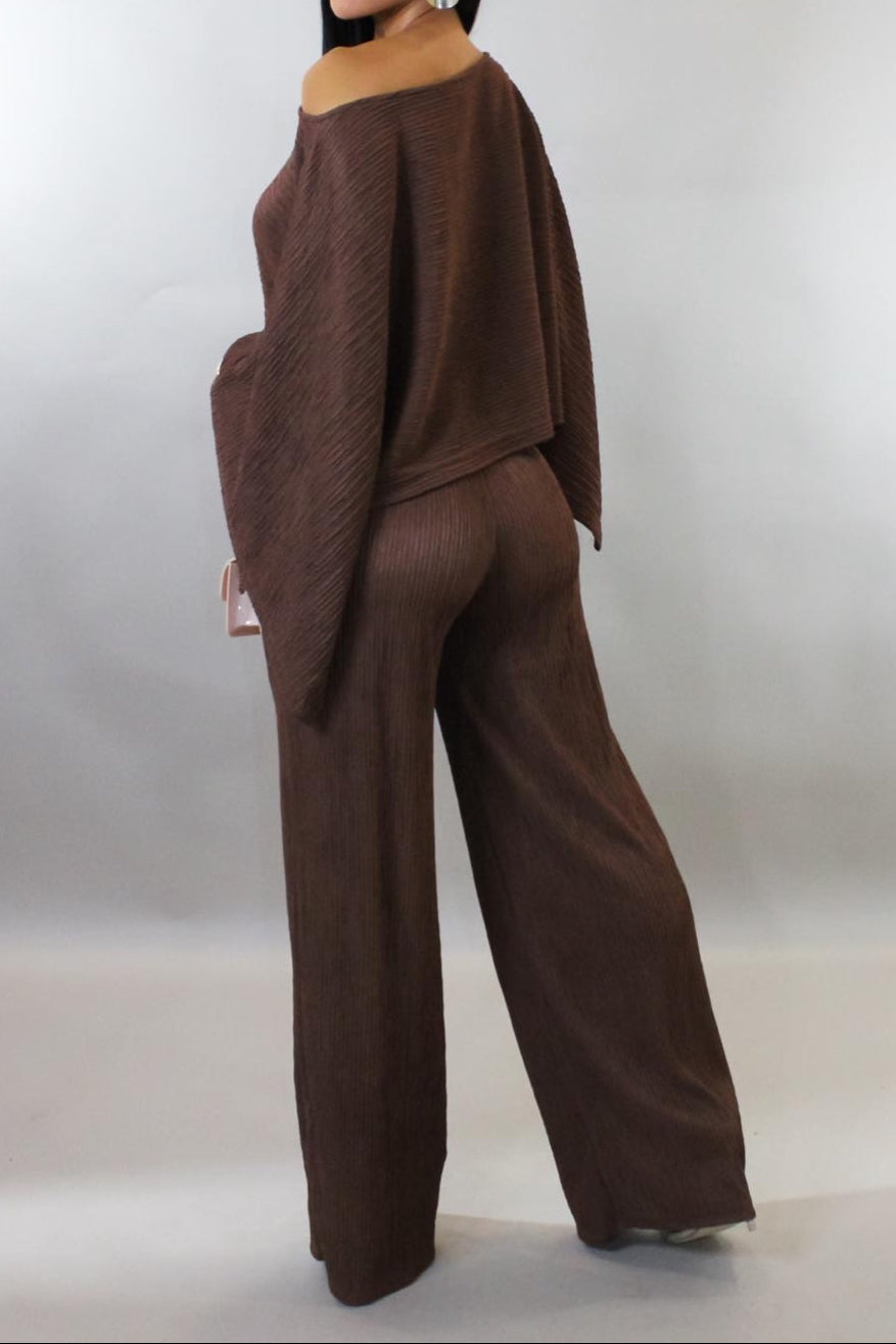 Woman wearing a brown outfit with a draped top and wide-leg pants on a plain background