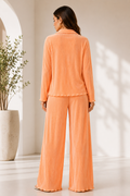 Woman wearing an orange pajama set in a bright room with a plant.