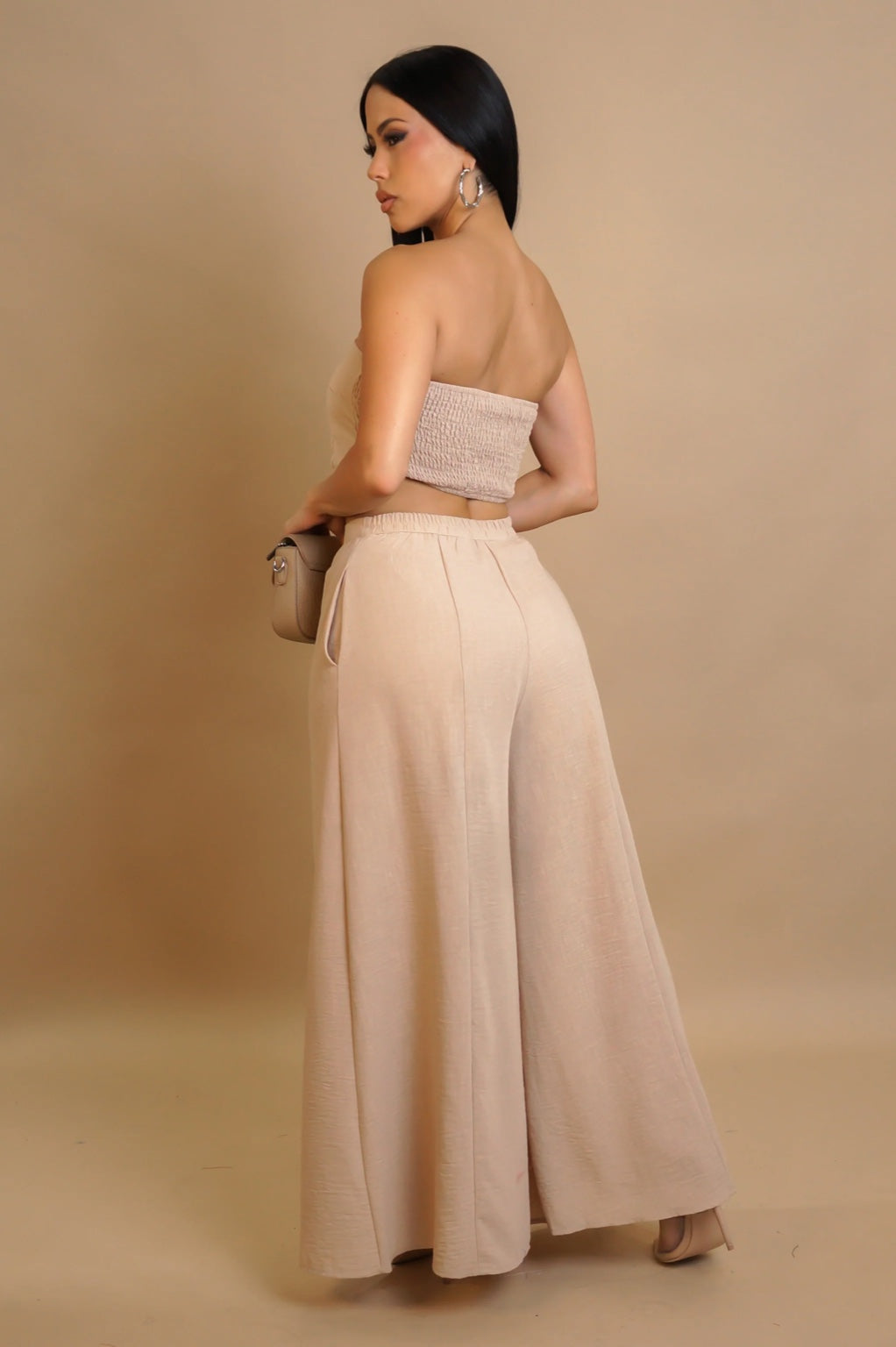 Woman wearing a beige strapless top and wide-leg pants against a beige background