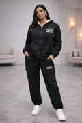 Woman wearing a black tracksuit with 'alo' logo in a modern indoor setting