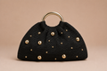 Black handbag with gold studs and handle on a beige background