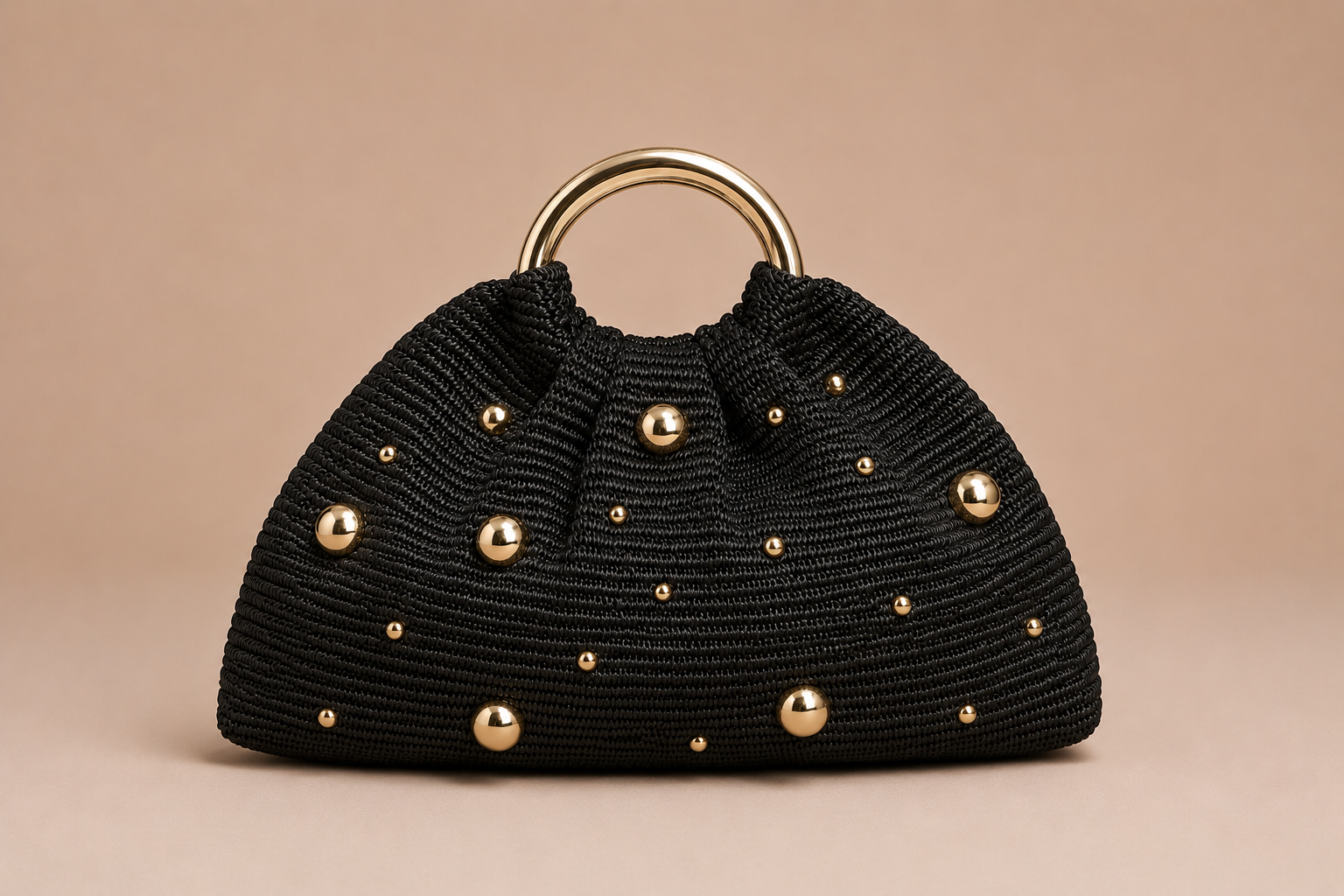 Black handbag with gold studs and handle on a beige background