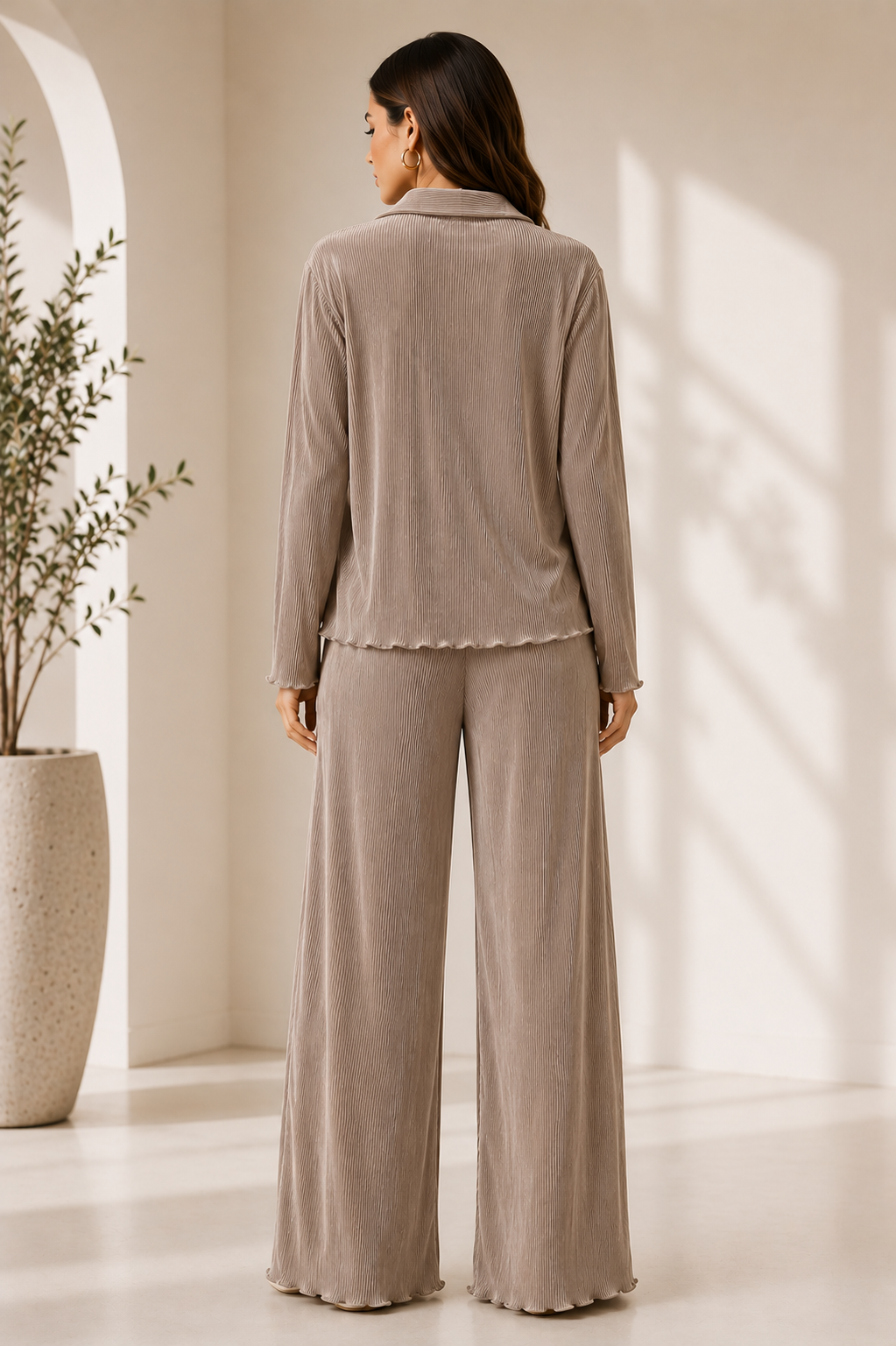 Woman wearing a beige button-up shirt and wide-leg pants in a bright room with a plant.
