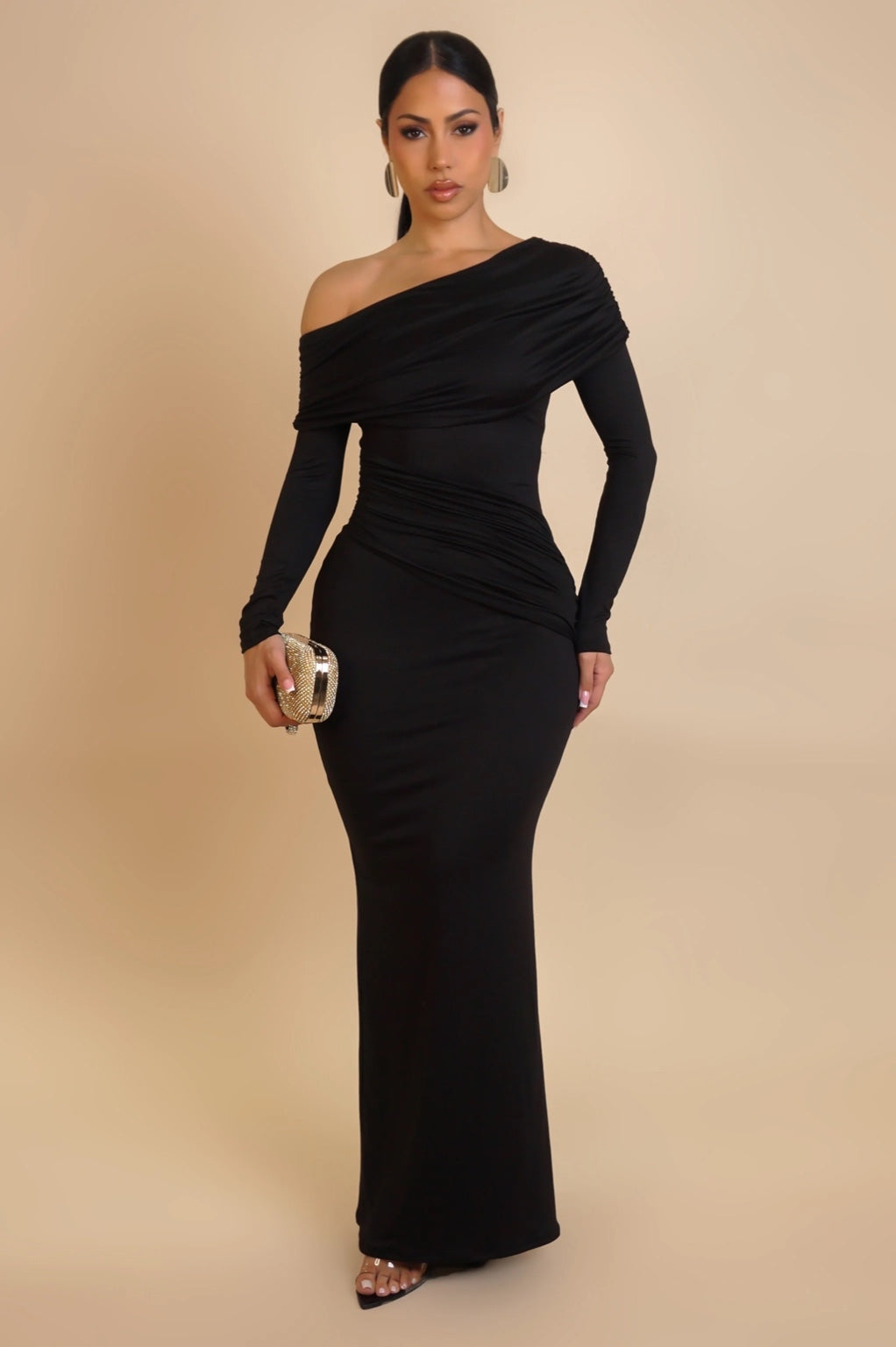 Woman in a black off-shoulder dress standing in an outdoor setting with columns and plants.