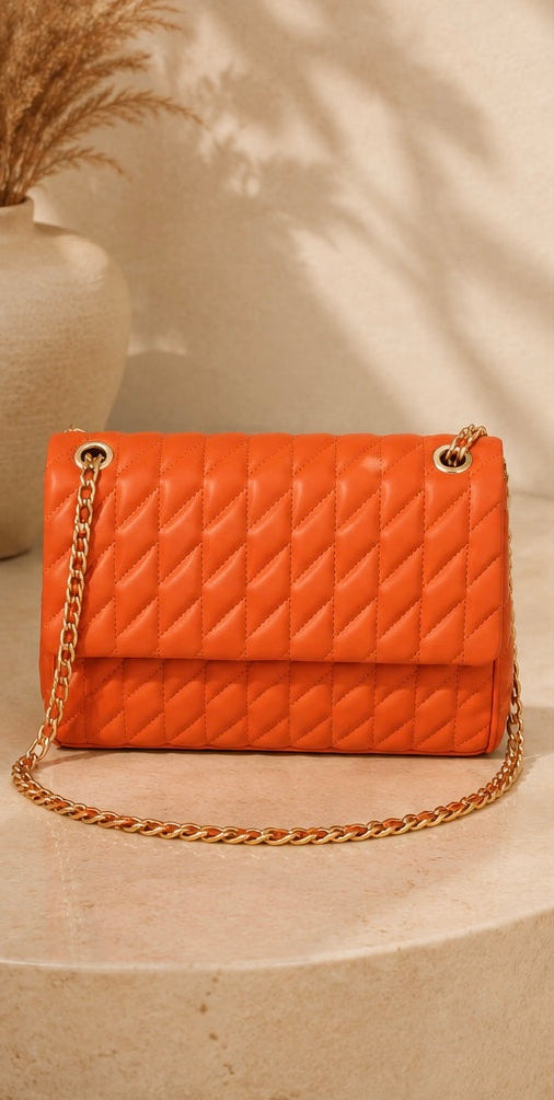 Orange quilted handbag with gold chain on a beige surface