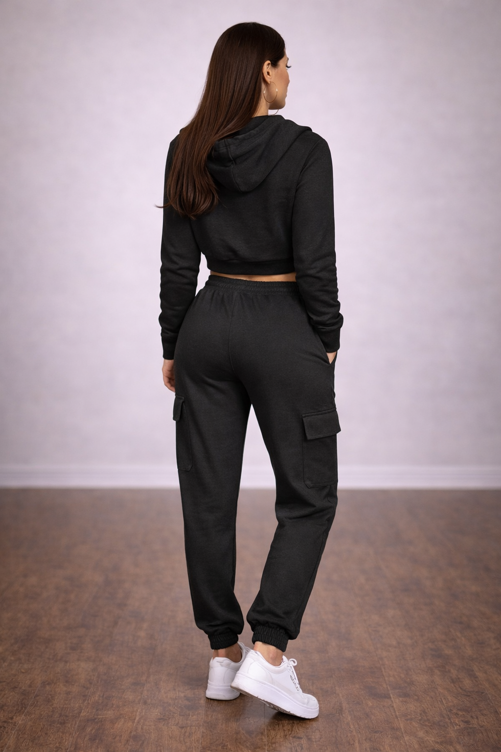 Person wearing a black tracksuit with white sneakers on a plain background