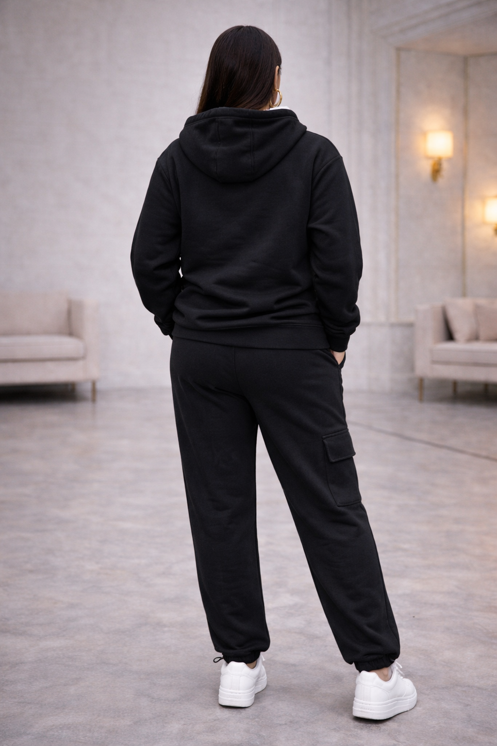 Woman wearing a black tracksuit with 'alo' logo in a modern indoor setting