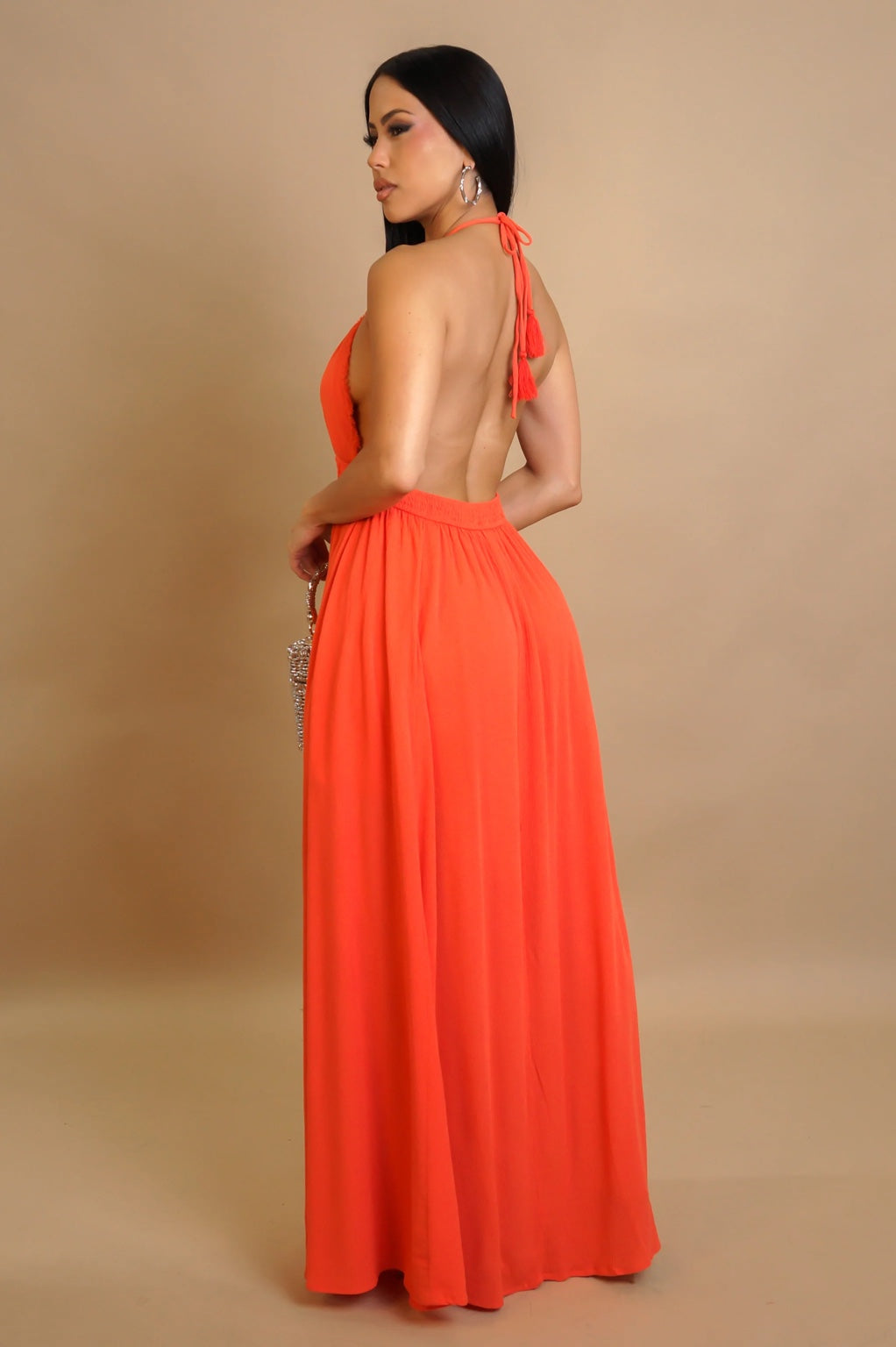 Woman wearing a bright orange halter neck dress against a beige background