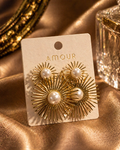 Gold earrings with pearl centers on a 'AMOUR' branded card against a gold fabric background