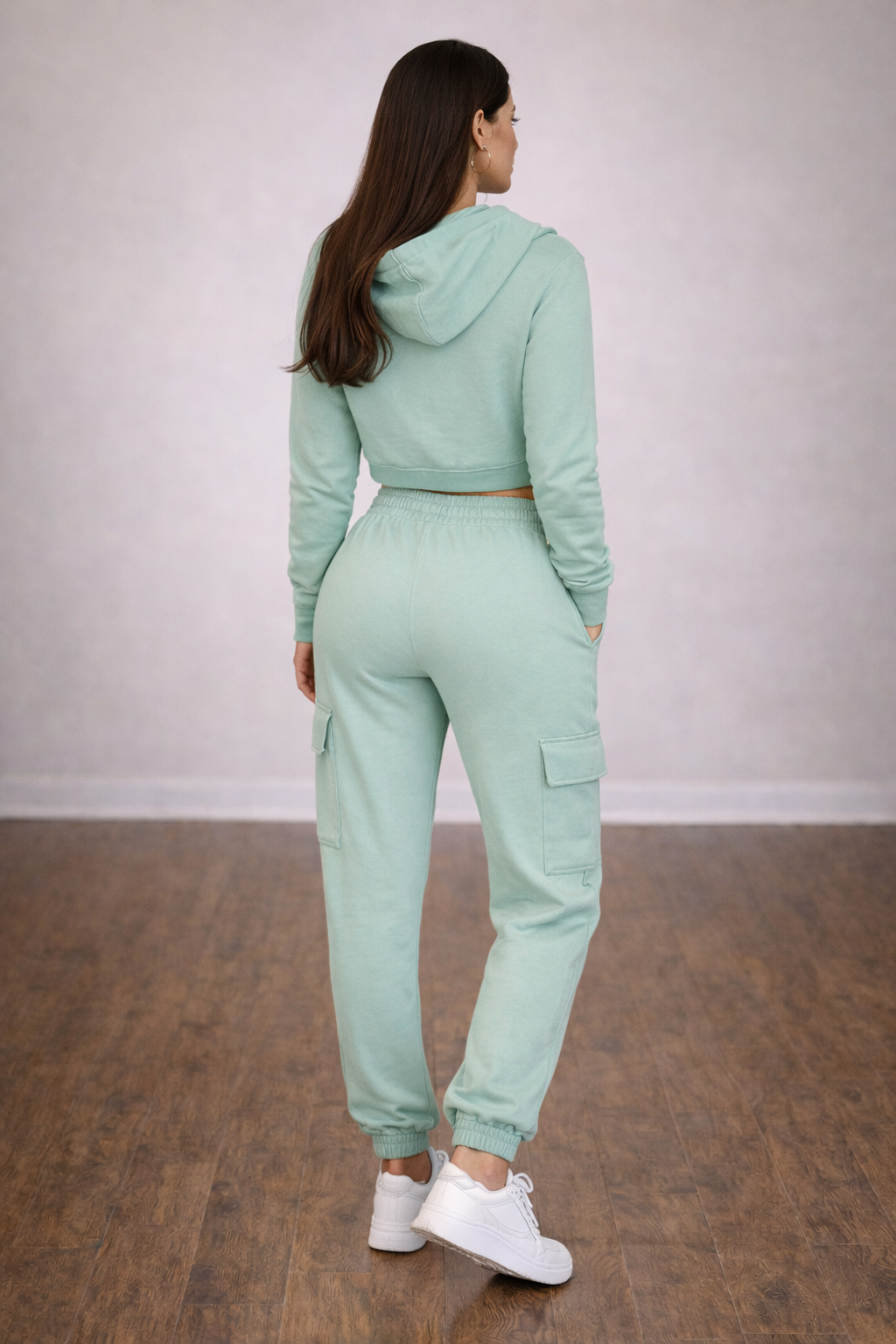 Person wearing a mint green tracksuit standing on a wooden floor with a plain background