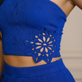 A close-up of a person wearing a bright royal blue ribbed knit crop top with a large floral cutout motif at the center, paired with a matching high-waisted bottom.