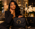  “Woman in black blazer resting hand on black Luxe Maison leather crossbody bag with gold ring buckle”