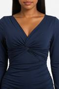 A close-up of a woman wearing a navy blue long-sleeve dress with a twisted V-neck detail at the center chest, shown against a plain light background.