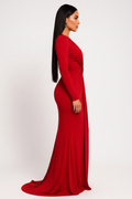 A woman modeling a long-sleeve, floor-length red gown in a side profile view against a plain white studio background.