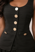 Close-up of a sleeveless black textured vest with large round beige buttons down the front and on the pockets, shown on a model.