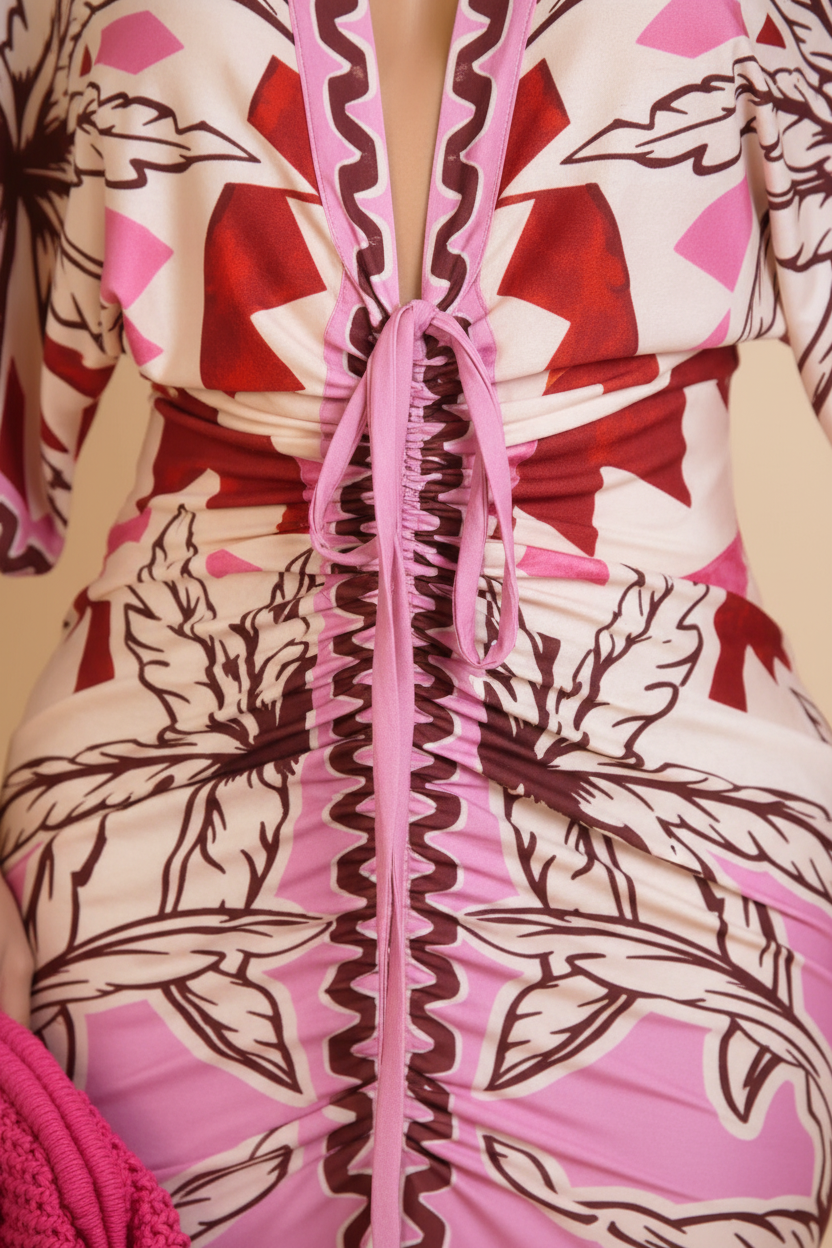 Close-up of a ruched wrap dress featuring a pink, red, and white floral print with a central tie closure.