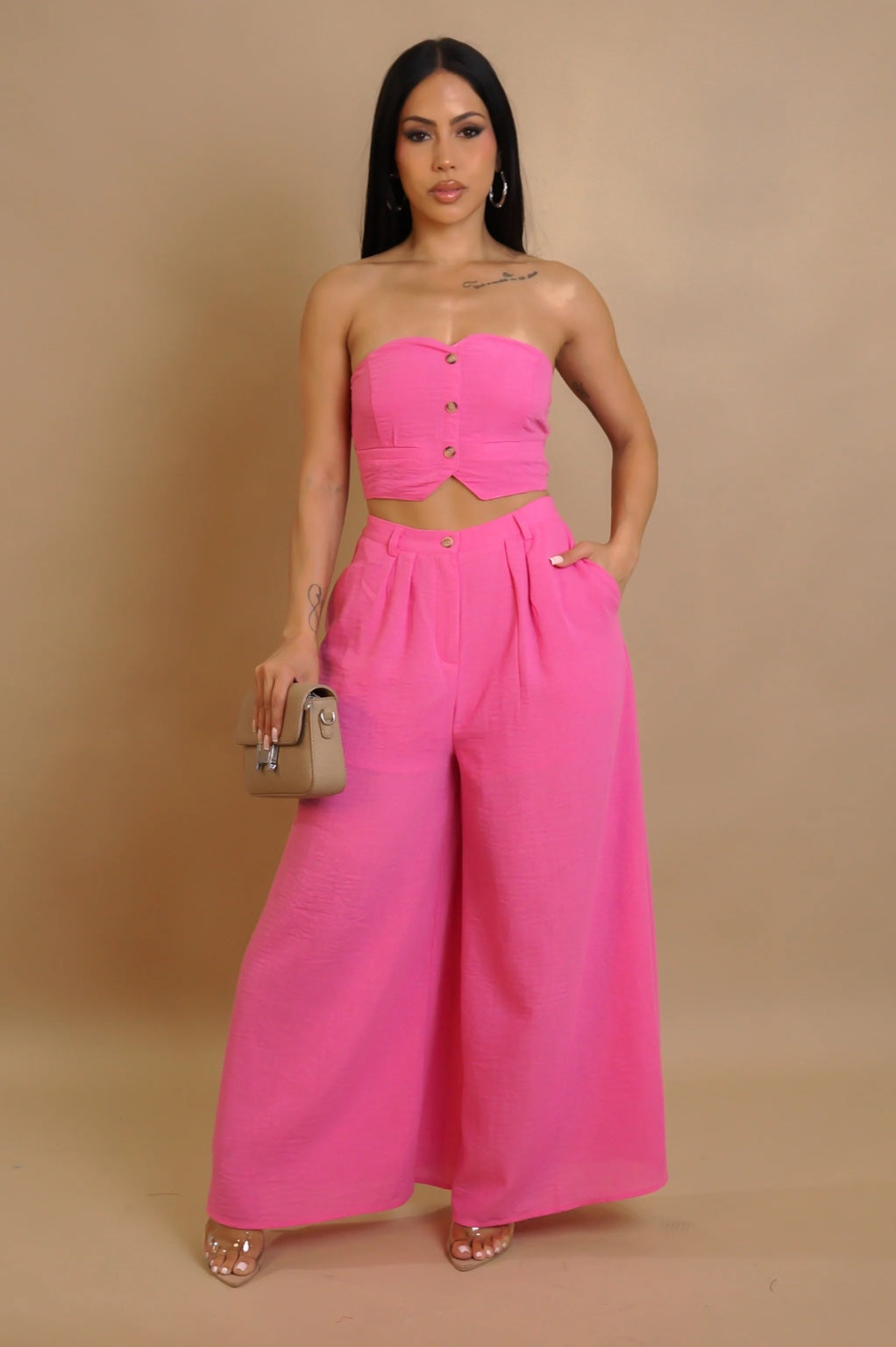 Woman wearing a bright pink strapless top and wide-leg pants against a beige background