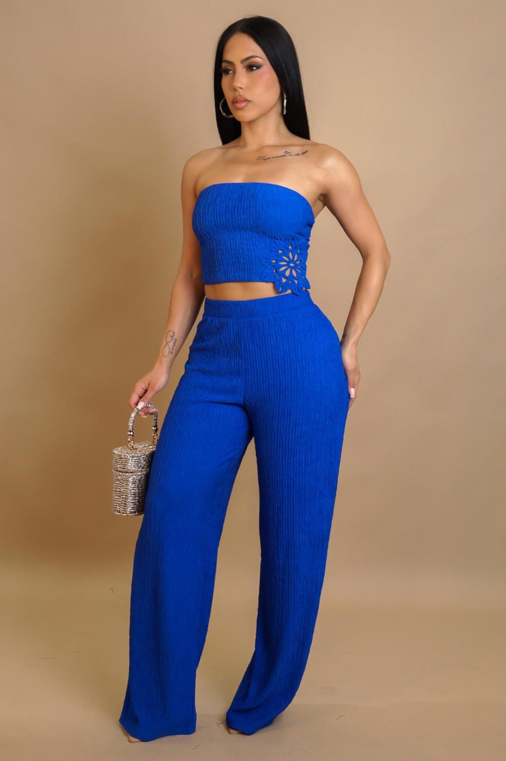 Woman wearing a blue strapless top and high-waisted pants against a beige background