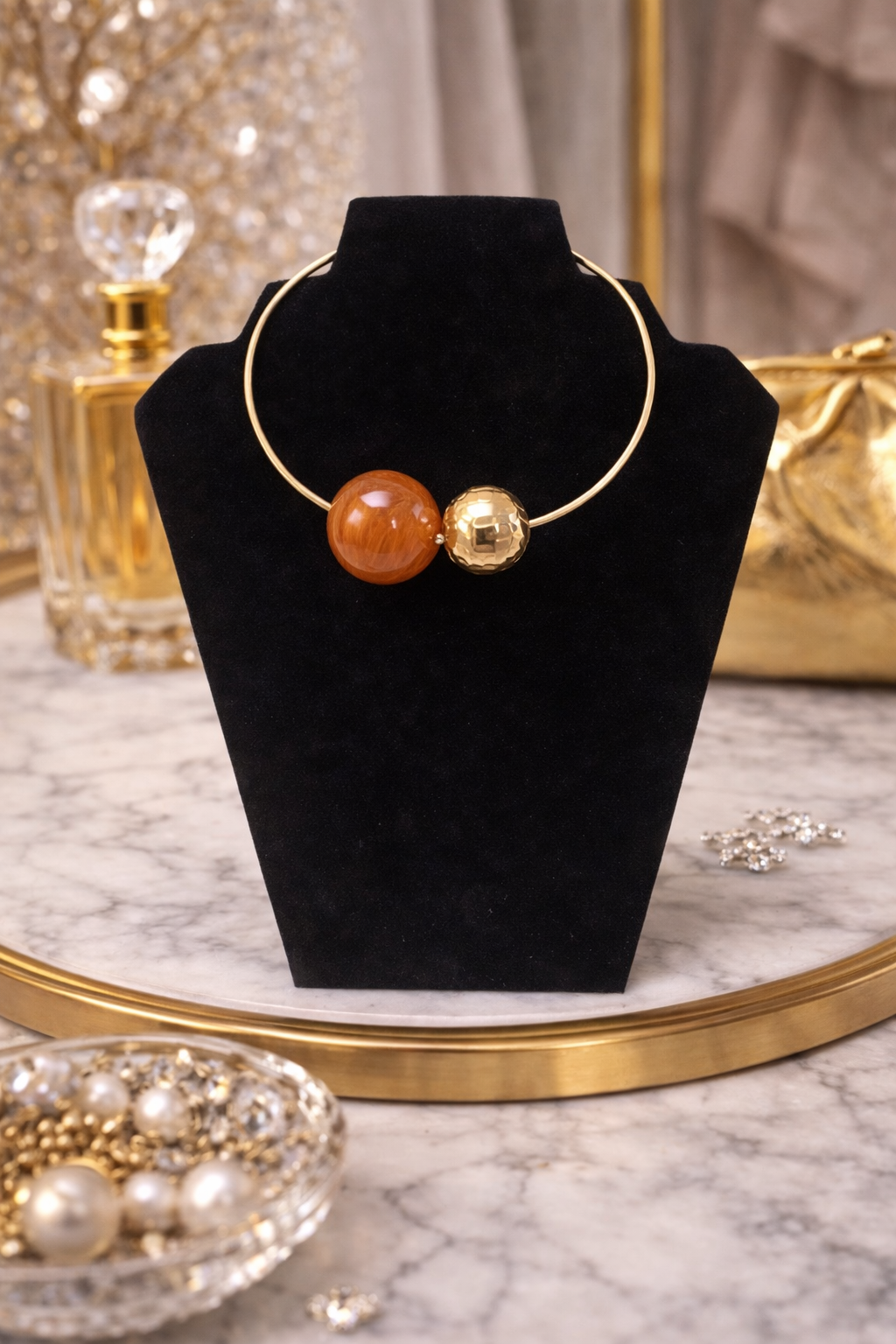 Necklace with gold and orange beads on a black stand with a marble background