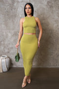 Woman wearing a green ribbed outfit against a gray concrete wall.