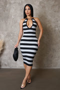Woman wearing a black and white striped dress against a gray concrete wall.