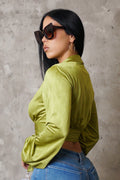 Woman wearing a green velvet top and blue jeans against a gray concrete wall.