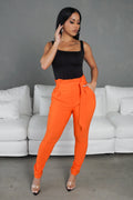 Woman wearing a black top and bright orange pants standing in front of a white sofa.