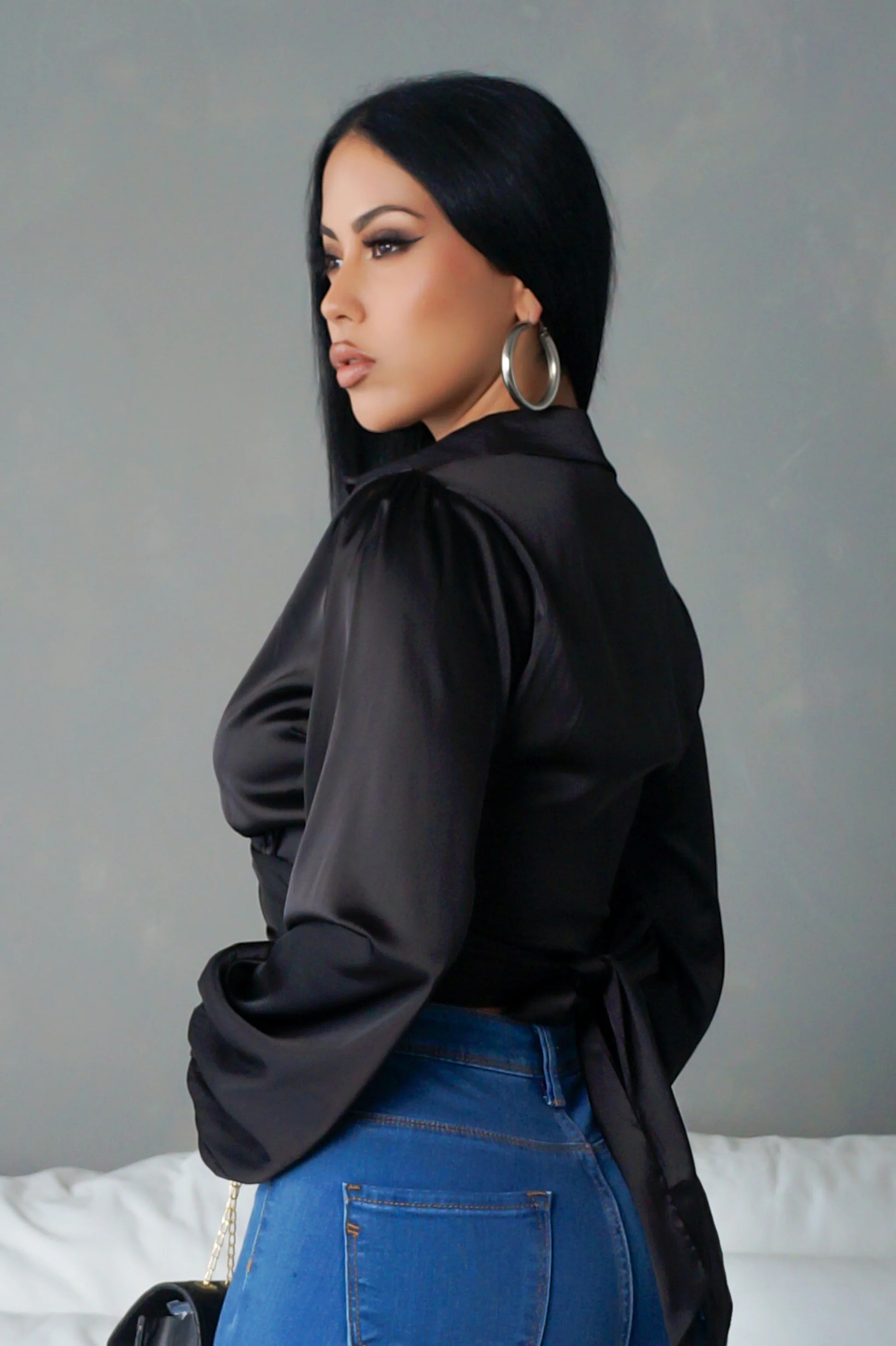 Woman wearing a black blouse and blue jeans against a gray background