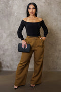 Woman wearing a black top and brown pants holding a clutch against a neutral background
