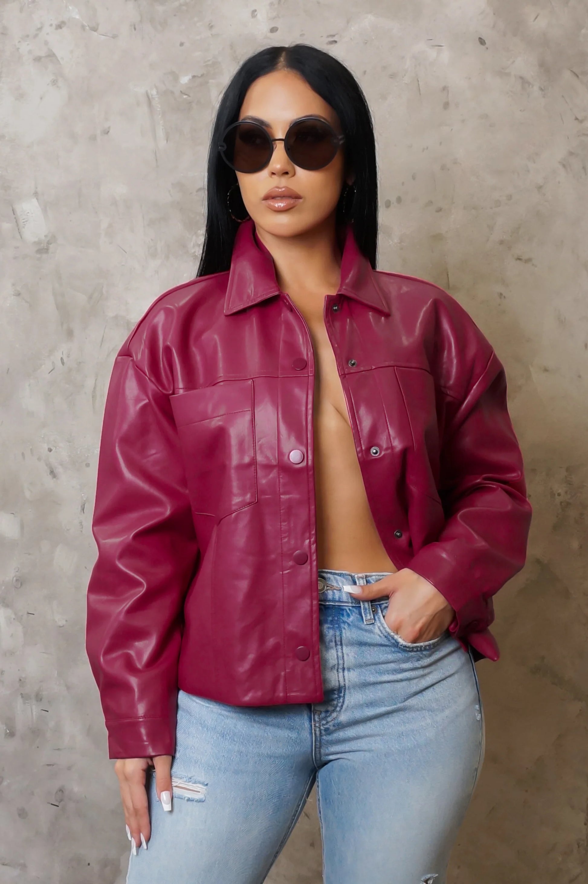 Woman wearing a red leather jacket and light blue jeans against a gray background