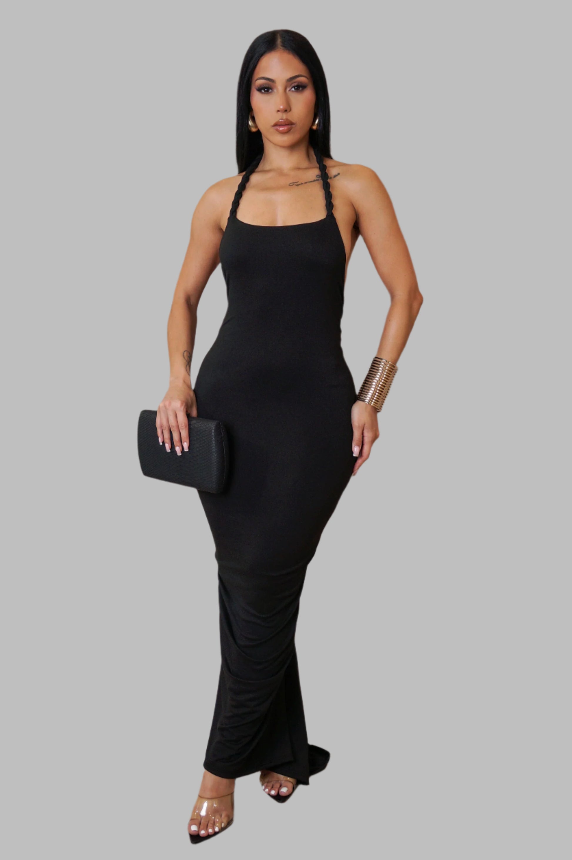 Woman wearing a black halter neck dress holding a black clutch against a gray background