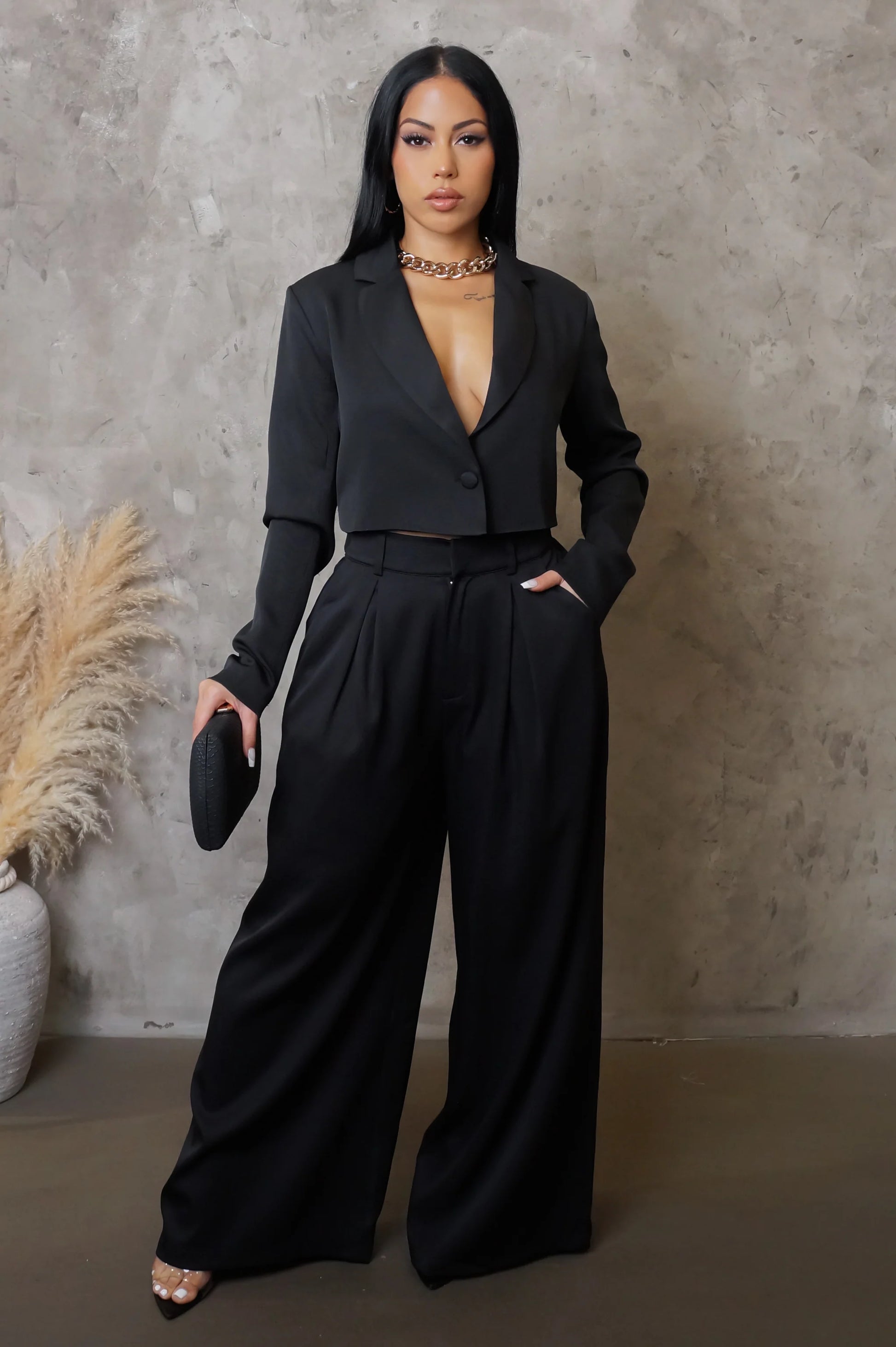 Woman wearing a black suit standing against a textured wall.