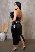 Woman in a black sequin dress standing against a textured wall with decorative elements.