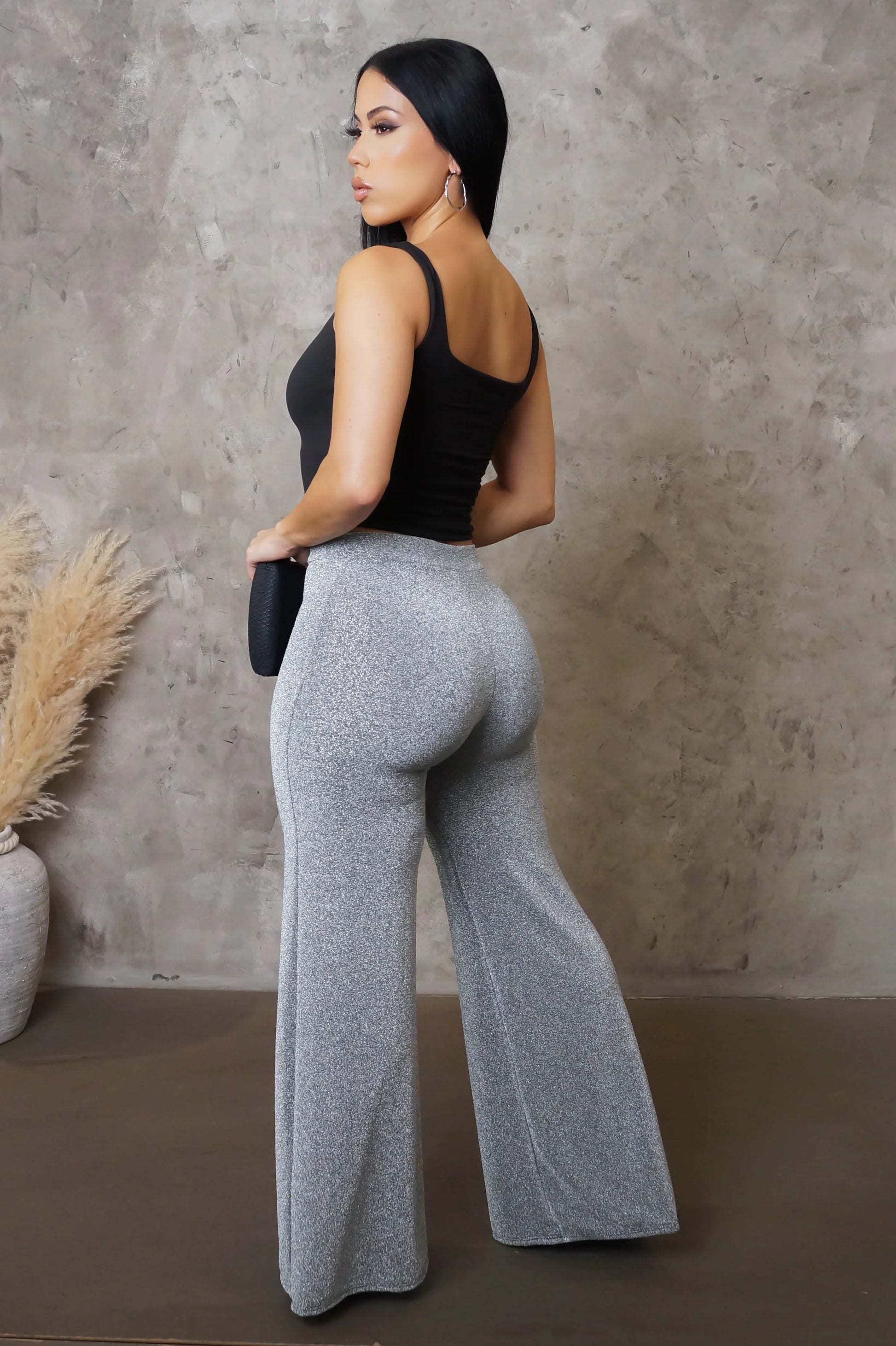 Woman wearing a black top and gray pants against a textured wall.