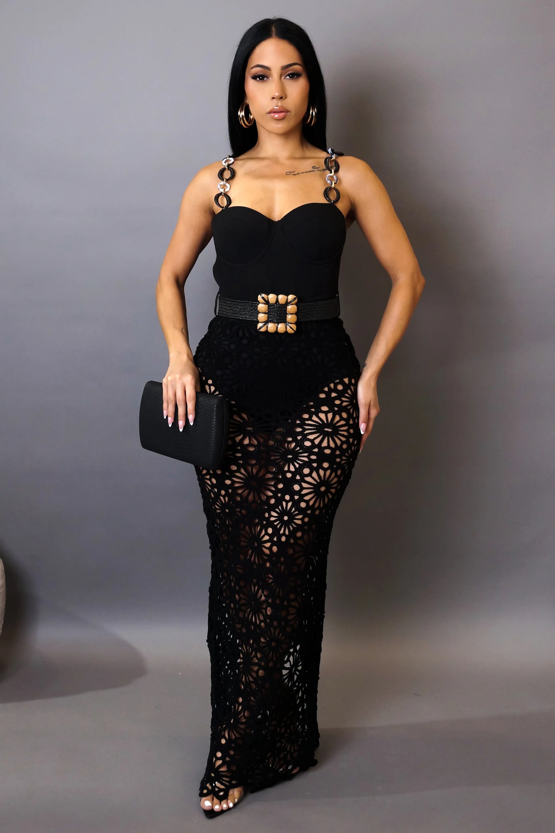 Woman wearing a black dress with cut-out design and belt on a gray background