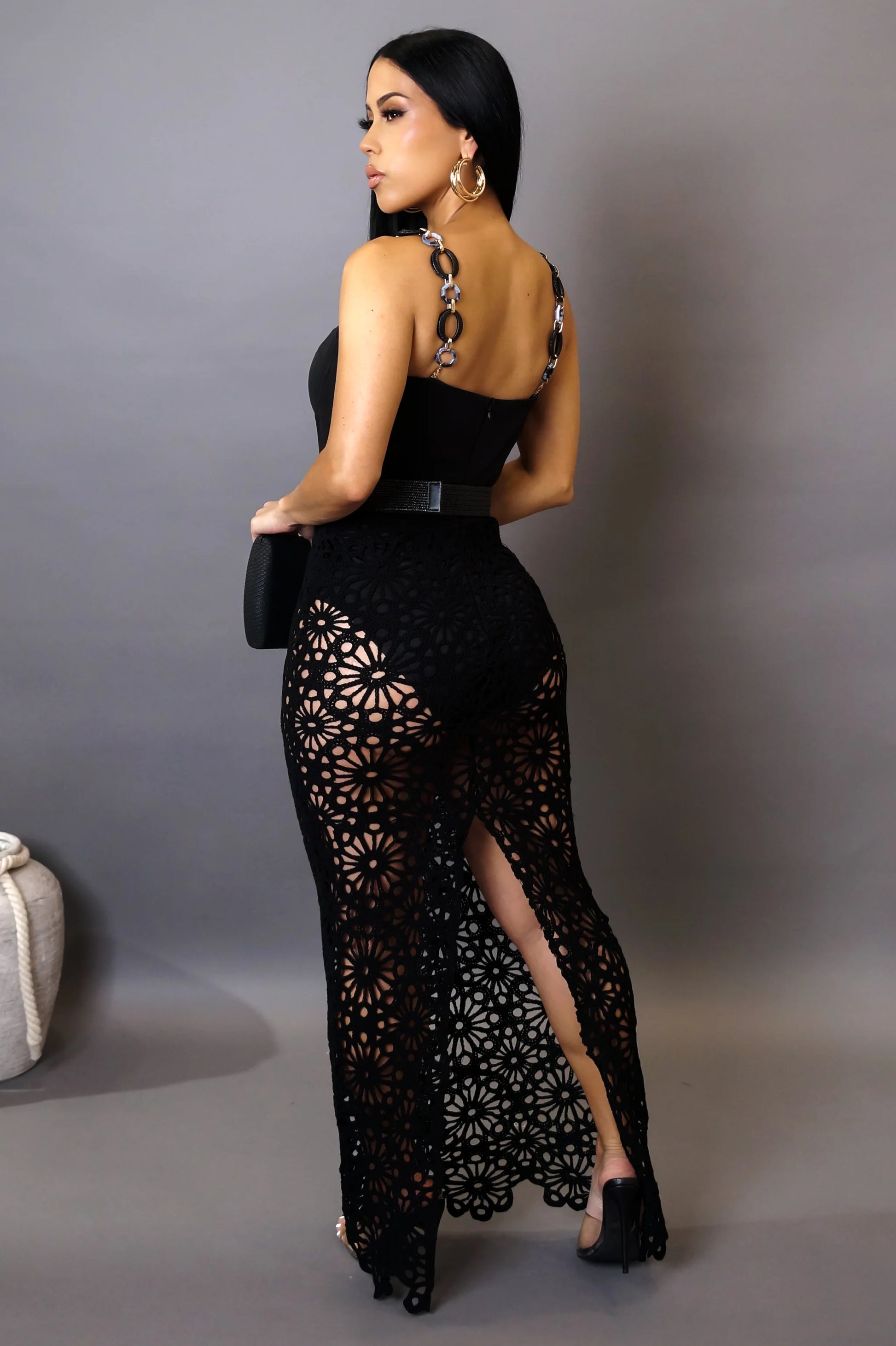 Woman wearing a black lace dress with a high slit on a gray background