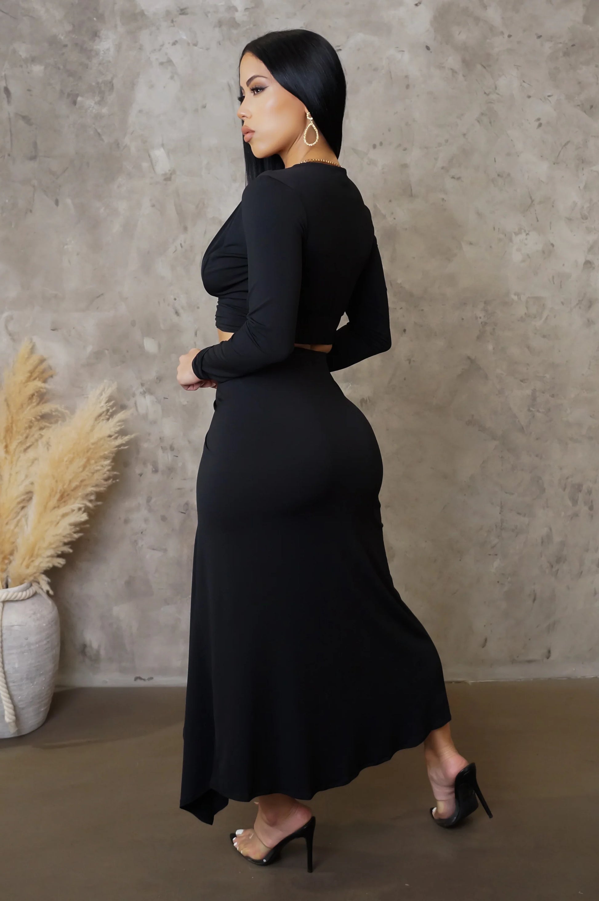 Woman in a black dress standing against a textured wall with decorative elements.