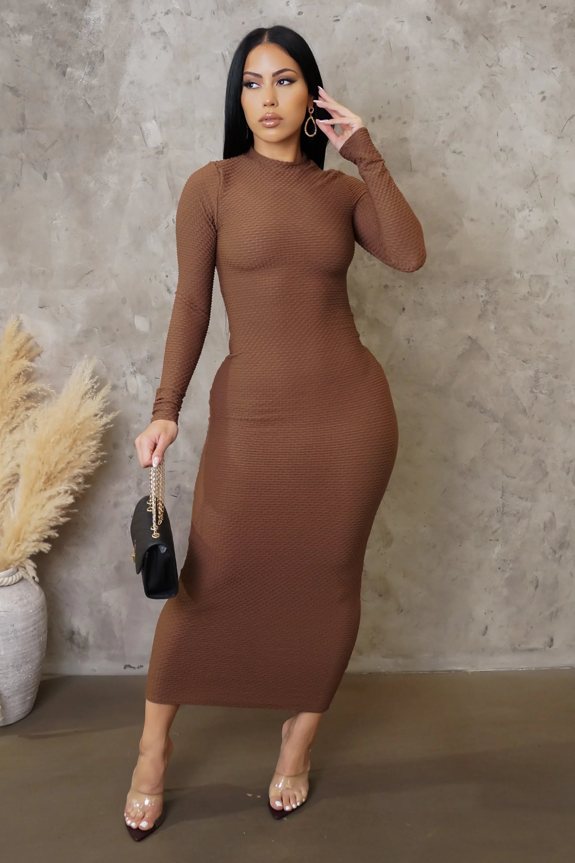 Woman wearing a brown dress against a textured wall.