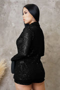 Woman wearing a black sequin outfit against a textured wall.