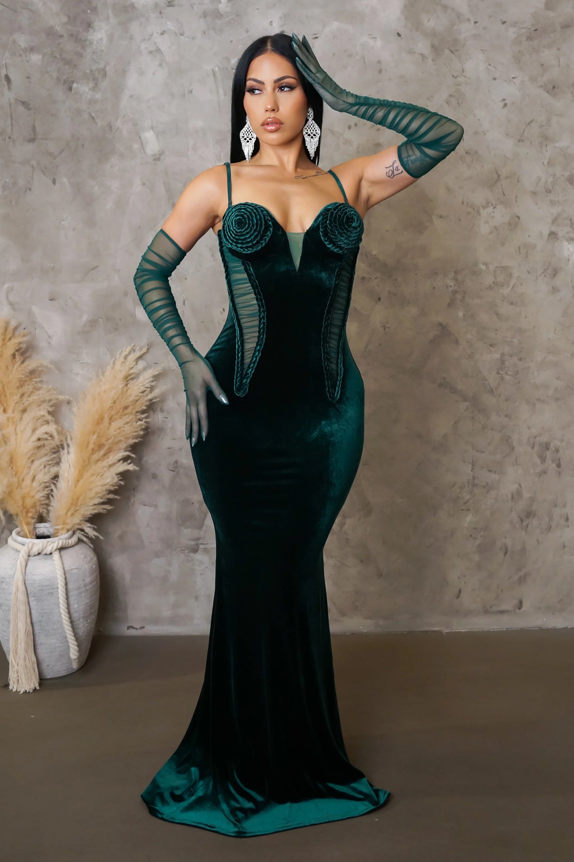 Woman in a green evening gown posing against a textured wall.