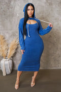 Woman wearing a blue ribbed dress and hood against a textured wall.