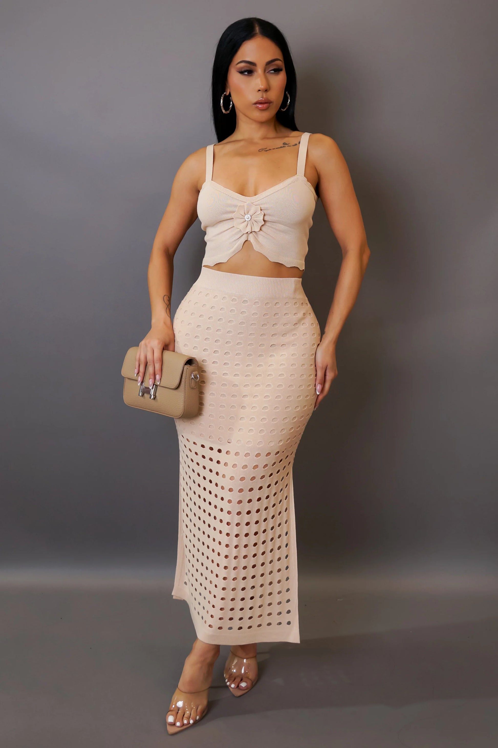 Woman wearing a beige top and skirt set with a clutch against a gray background